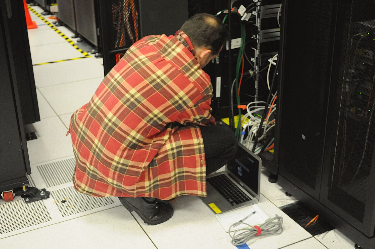 A technician with a laptop working at a rack of servers in a data centre